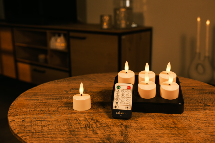 Zes oplaadbare beste led waxinelichtjes 2026 (75 uur brandtijd) met afstandsbediening staan op een ronde houten tafel in een sfeervolle kamer, ideaal voor ontspannen avonden.