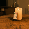 Een Oplaadbare led kaars (7,5cm x 12,5 cm, 30 uur brandtijd) met afstandsbediening staat op een ronde houten tafel in een warm verlichte kamer, met soft-focus meubels en zacht gloeiende kaarsen op de achtergrond.