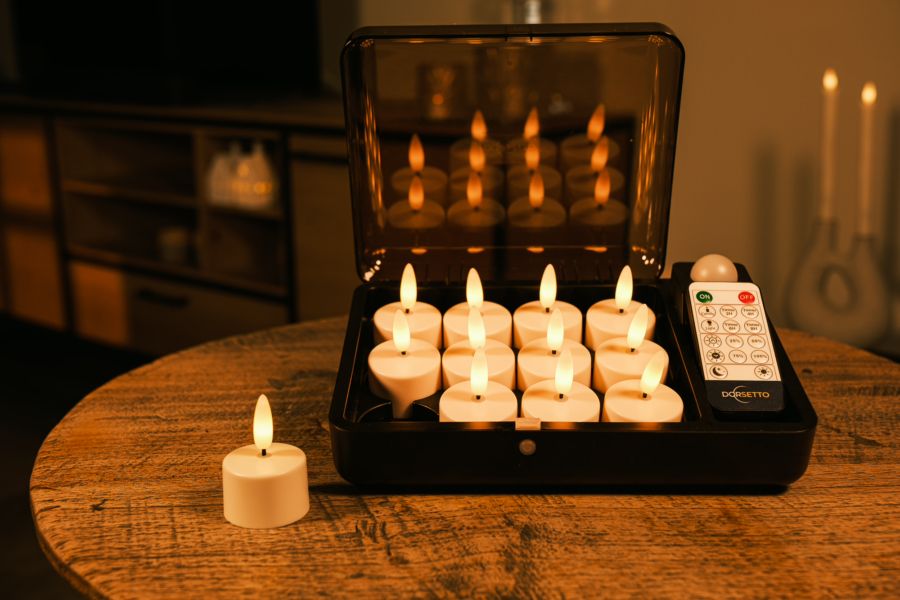 Een set van 12 oplaadbare waxinelichtjes met afstandsbediening en 3D vlam (tot 400 uur merkduur), in een zwarte opbergkist op een houten tafel; één kaars is buiten de kist geplaatst.
