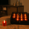 Een gezellige, zacht verlichte kamer met een tafelbladspel met negen rode oplaadbare waxinelichtjes uit een set van 12 realistische, waterdichte LED theelichtjes (tot 400 uur brandduur, timerfunctie), plus een kaars buiten het rooster op een houten tafel.