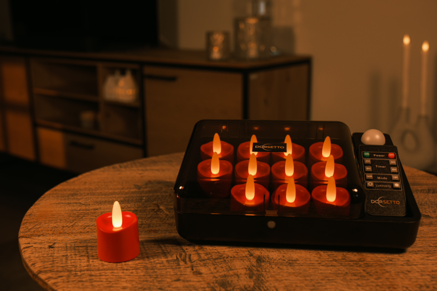 Een gezellige, zacht verlichte kamer met een tafelbladspel met negen rode oplaadbare waxinelichtjes uit een set van 12 realistische, waterdichte LED theelichtjes (tot 400 uur brandduur, timerfunctie), plus een kaars buiten het rooster op een houten tafel.