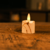 Een Realistisch led waxinelichtje oplaadbaar - marmer look zit op een houten oppervlak, de warme gele gloed trekt de aandacht terwijl de wazige achtergrond het marmeren ontwerp benadrukt.