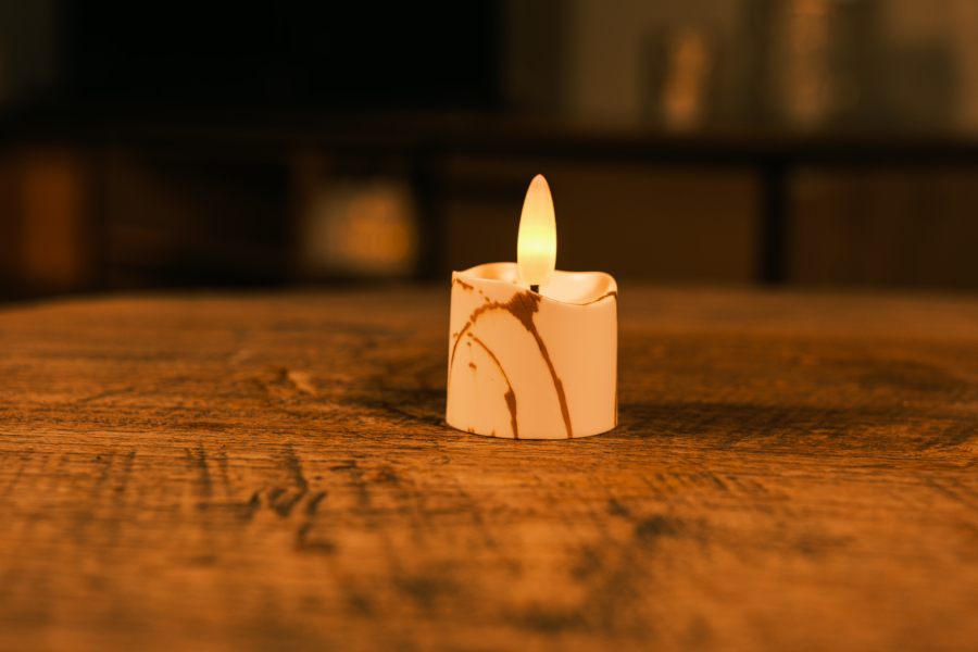 Een Realistisch led waxinelichtje oplaadbaar - marmer look zit op een houten oppervlak, de warme gele gloed trekt de aandacht terwijl de wazige achtergrond het marmeren ontwerp benadrukt.