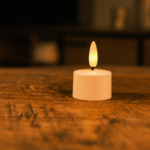 Een 1 oplaadbaar led waxinelichtje met timerfunctie (175 uur brandtijd, los) staat op een houten tafel en zorgt voor een warme, gezellige sfeer. De achtergrond is onscherp.