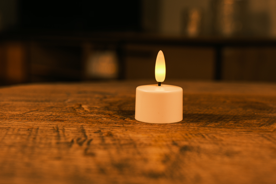 Een 1 oplaadbaar led waxinelichtje met timerfunctie (175 uur brandtijd, los) staat op een houten tafel en zorgt voor een warme, gezellige sfeer. De achtergrond is onscherp.
