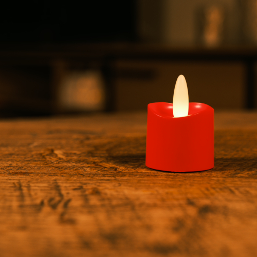 Een enkele oplaadbare rode LED theelichtje kaars met een realistische vlam (waterdicht, brandtijd 175 uur) verlicht zachtjes een houten tafel in een schemerige kamer.