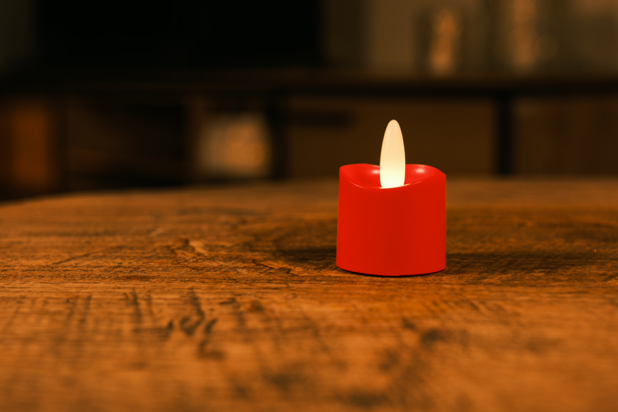 Een enkele oplaadbare rode LED theelichtje kaars met een realistische vlam (waterdicht, brandtijd 175 uur) verlicht zachtjes een houten tafel in een schemerige kamer.