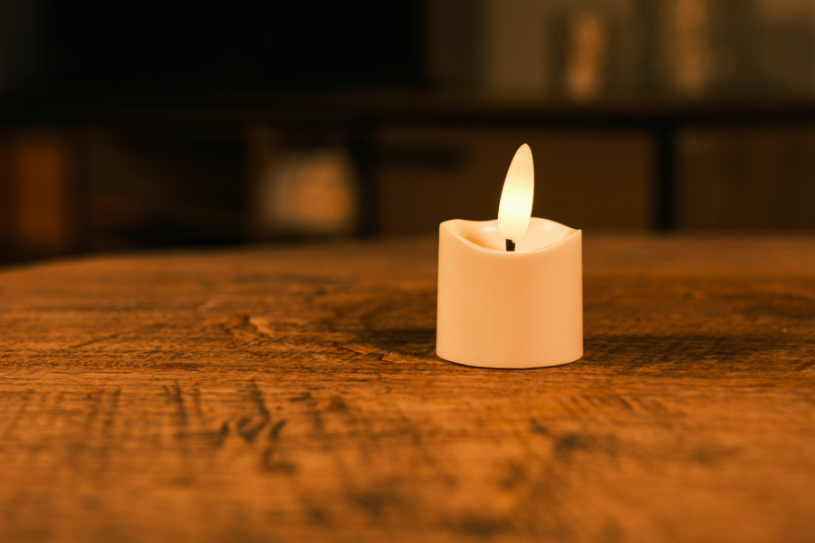 Het Realistisch led waxinelichtje oplaadbaar - los, een kleine witte led kaars met een gloeiende kunstmatige vlam, staat op een rustiek houten oppervlak tegen een zacht vervaagde achtergrond.