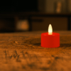 Een enkel waterdicht oplaadbaar rood LED theelichtje (brandduur 175 uur, wordt per stuk verkocht) gloeit zachtjes op een houten tafel in een zwak verlichte kamer met een onscherpe achtergrond.