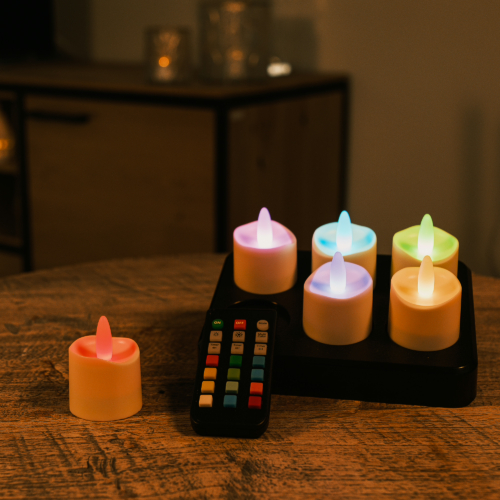 Een set van 6 oplaadbare waxinelichtjes, rgb, waterdicht, met afstandsbediening en timerfunctie (68 uur brandtijd) staat op een houten tafel met zwarte oplaadtray; één led kaars is apart geplaatst en klaar voor gebruik. Beste oplaadbare led verlichting 2026