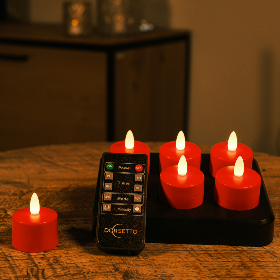 Zes rode oplaadbare LED-theelichtjes met afstandsbediening en timerfunctie, die 175 uur licht geven, staan op een houten tafel; vier zitten op een zwart oplaadplateau, één ernaast, terwijl op de achtergrond een schemerig verlicht kastje verschijnt.
