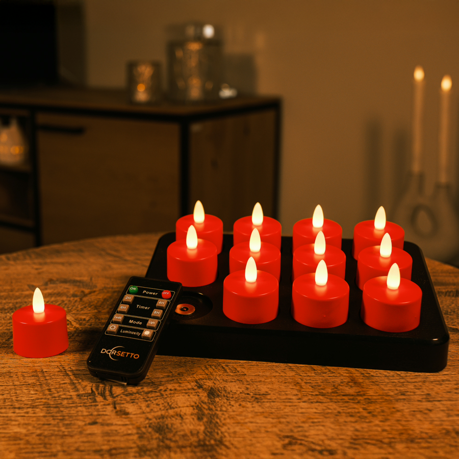 Een set van 12 waterdichte, oplaadbare waxinelichtjes met rode LED's en afstandsbediening staat op een zwarte laadschaal op een houten tafel; één kaarsje staat los. Ze bieden tot 175 uur brandtijd. De achtergrond is sfeervol ingericht.