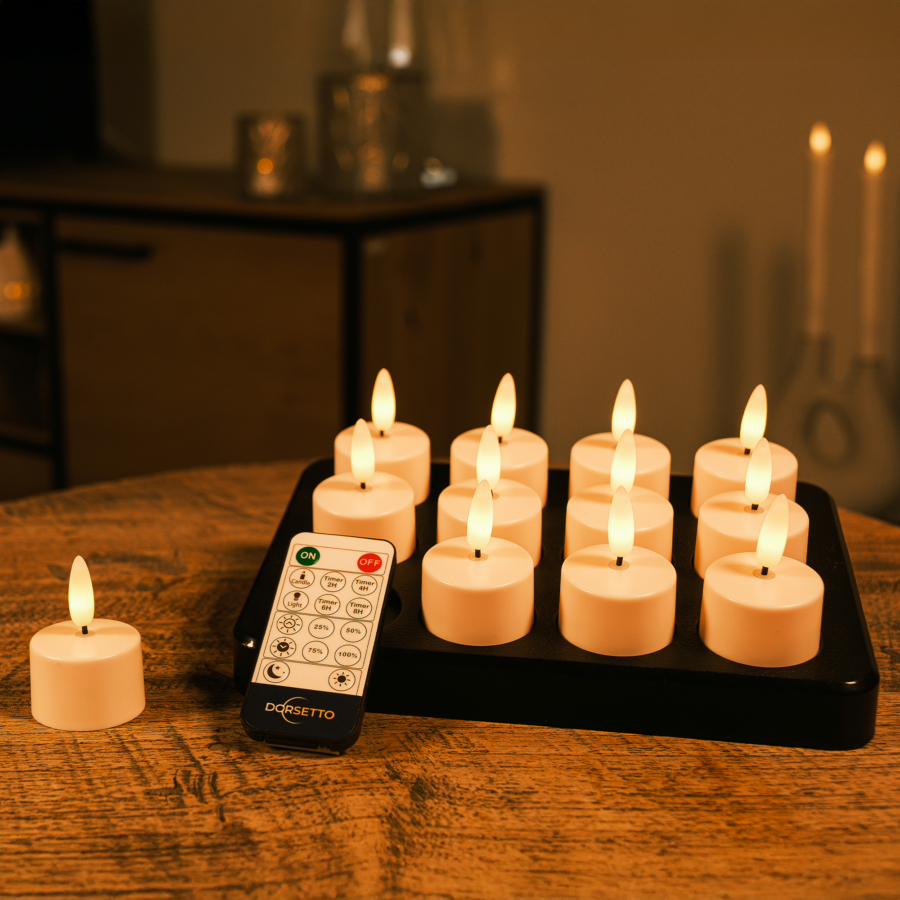 Een set van 12 oplaadbare waxinelichtjes met 3D vlam en 175 uur brandtijd staat op een tray, met afstandsbediening erbij. Eén kaars staat apart in een gezellige, sfeervol verlichte kamer.