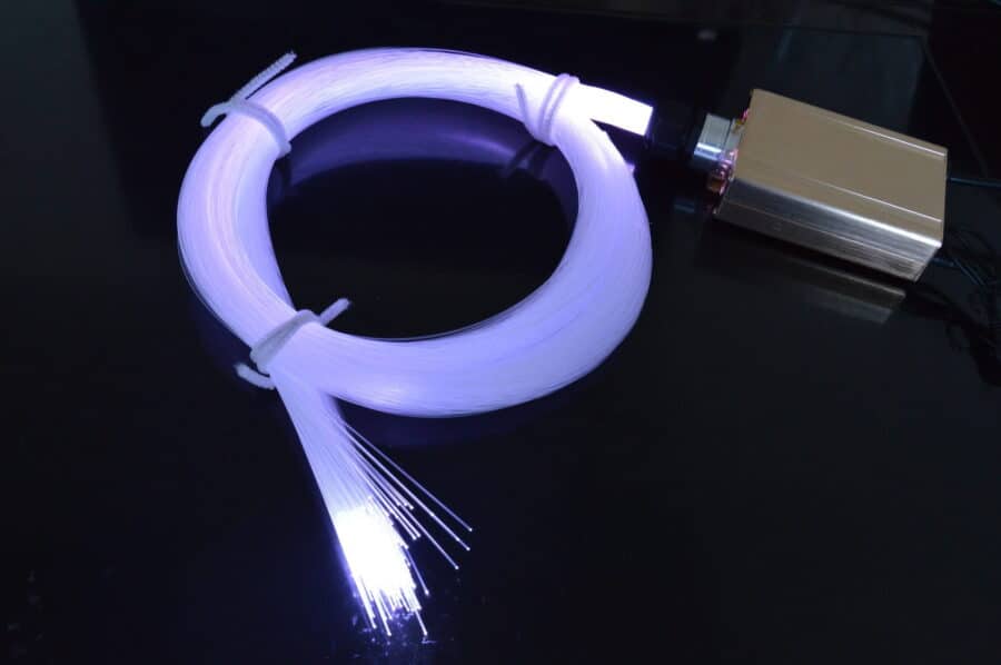 Een bundel gloeiende optische vezels, gelust en gebonden, straalt wit licht uit van de Sterrenhemel RGB 400 stuks met afstandsbediening lichtbron op een reflecterend zwart oppervlak.