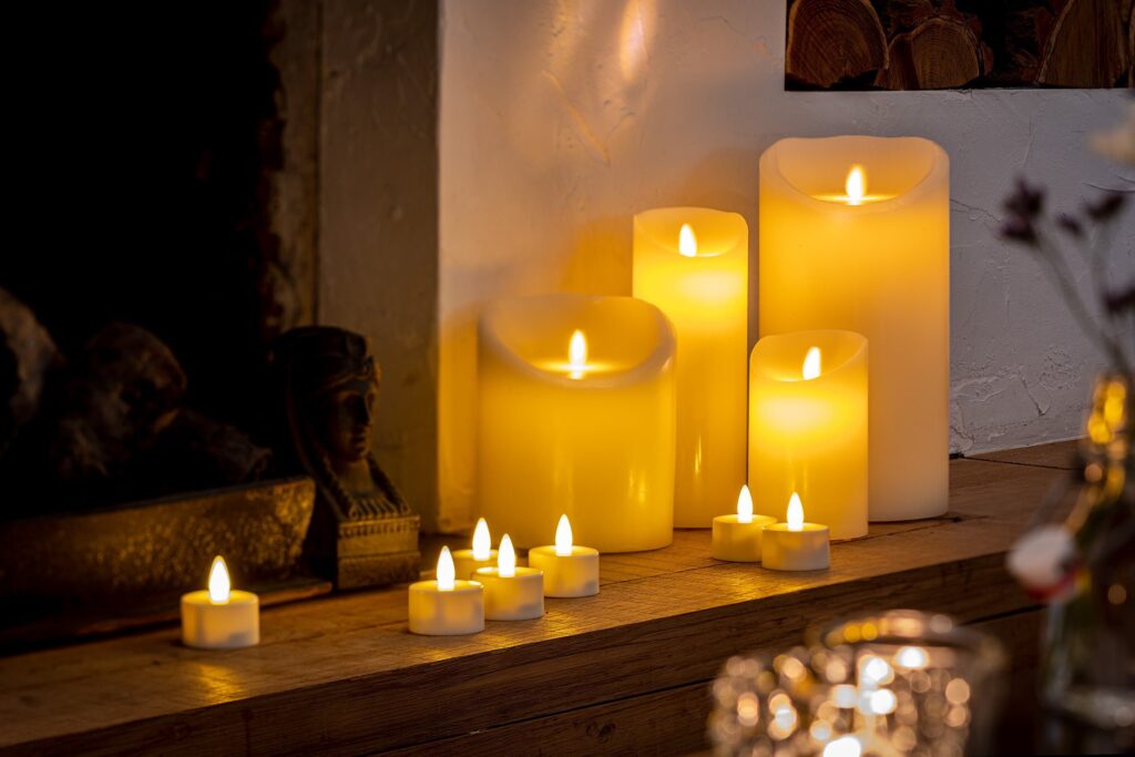 Een groep oplaadbare led kaarsen (7,5 cm x 20 cm, 30 uur brandtijd, met afstandsbediening) gloeit warm op een houten schoorsteenmantel en creëert een gezellige sfeer naast enkele kleine waxinelichtjes.