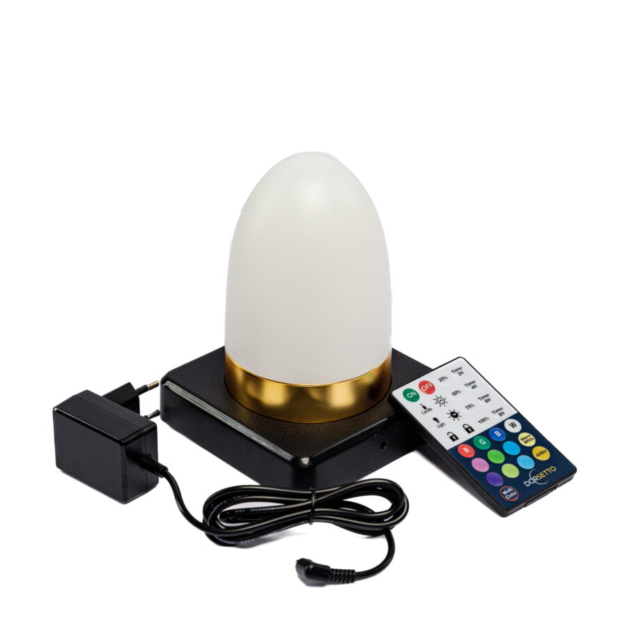 Een moderne, waterdichte, oplaadbare LED tafellamp in ovaal wit/goud met timerfunctie staat op een zwart plateau. Ernaast ligt een afstandsbediening met gekleurde knoppen en een zwarte stroomadapter met opgerolde kabel.