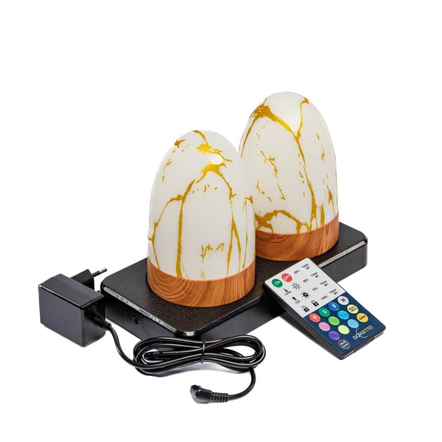De DORSETTO oplaadbare tafellampen (set van 2, ovaal, marmer goud) met houten voet staan op een zwarte oplaadvoet. Een afstandsbediening en stroomadapter zitten naast de voet. Elke lamp is waterdicht en gaat tot 105 uur mee.