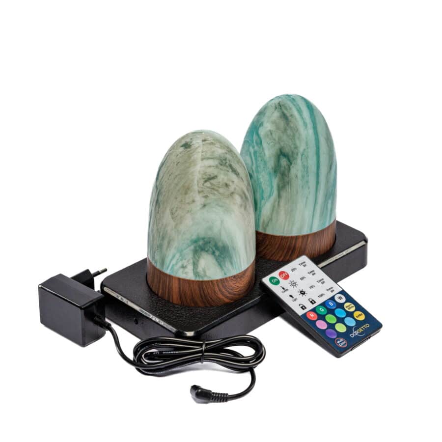 Twee ovale, groen marmeren, oplaadbare LED tafellampen met houteffect voet en timer staan op een zwart plateau, met een zwarte voedingsadapter en veelkleurige afstandsbediening ervoor.