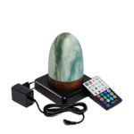 Deze stijlvolle oplaadbare led tafellamp heeft een ovaal marmergroen ontwerp met een houtlook voet en een timerfunctie. Hij is waterdicht en oplaadbaar en wordt geleverd met een afstandsbediening en zwarte adapter, gepresenteerd op een zwart plateau.