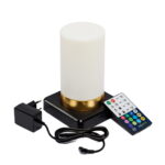 Een cilindervormige oplaadbare led tafellamp in wit met goudlook staat op een zwarte ondergrond, vergezeld van een zwarte adapter en een kleurrijke afstandsbediening voor instellingen. De lamp is waterdicht en heeft een timerfunctie.