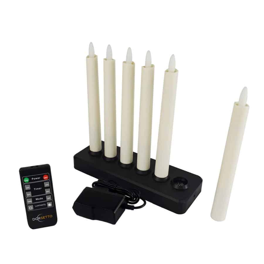 Zes warmwitte, 197 mm oplaadbare dinerkaarsen (brandduur 130 uur) staan rechtop in een zwarte oplaadhouder, eentje ligt ernaast. Een AC-adapter en de gelabelde afstandsbediening liggen vlakbij.
