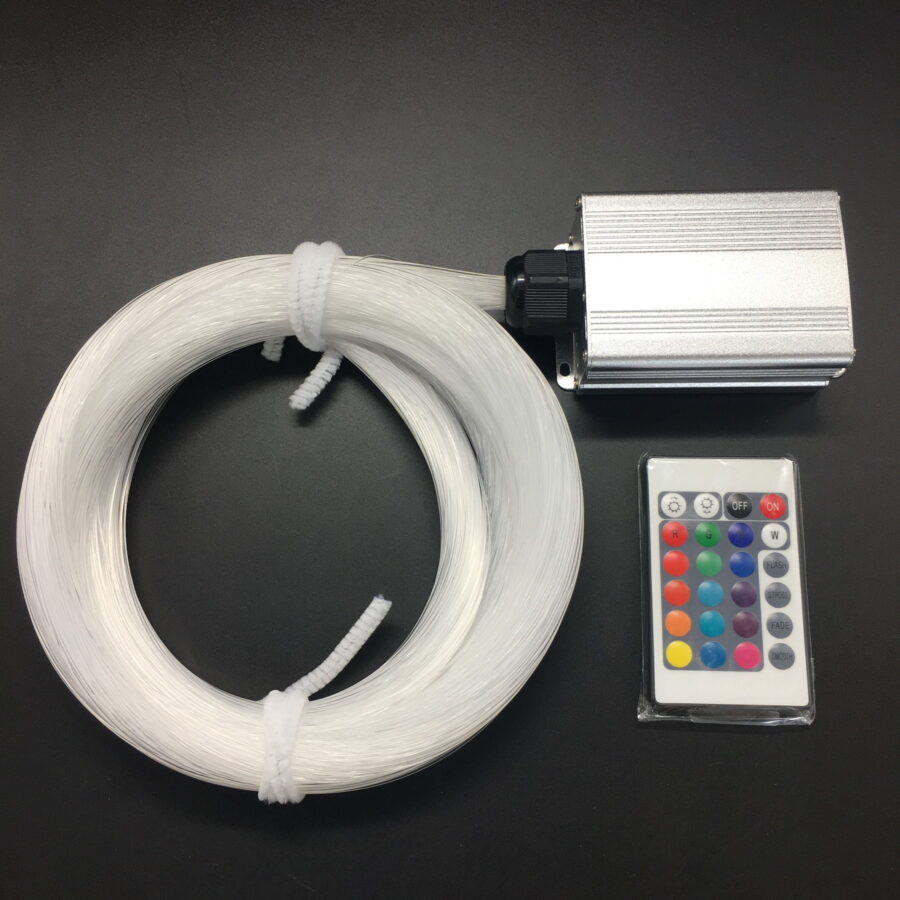 De LED Sterrenhemel RGB (180 sterren) met afstandsbediening bestaat uit een opgerolde bundel transparante glasvezelkabels, een compacte metalen controllerbox en een afstandsbediening met kleurrijke knoppen, allemaal weergegeven op een zwart oppervlak.