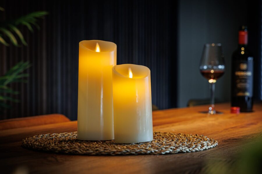 Twee oplaadbare led kaarsen (set van 2, 30 uur brandtijd, met afstandsbediening, timer- en dimfunctie) verspreiden warm licht op een houten tafel en zorgen zo voor een gezellige, uitnodigende sfeer.