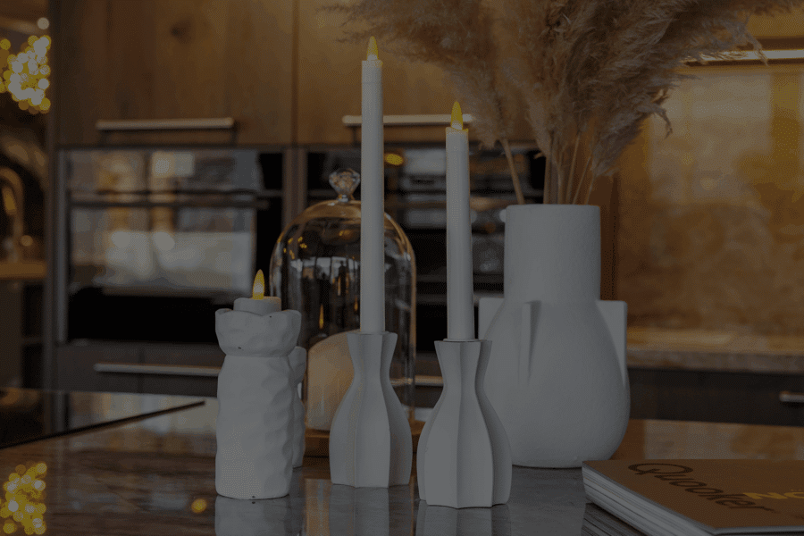 Een modern aanrecht met witte decoratieve vazen, twee brandende witte kaarsen, droog pampagras in een vaas, een glazen cloche en een boek met de titel Citaten in de hoek.