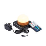 Een witte, waterdichte, oplaadbare LED tafellamp in een ronde vorm met houtlook voet staat op een zwart plateau, afgebeeld met een afstandsbediening met kleurrijke knoppen en een zwarte voedingsadapter met snoer. Inclusief timerfunctie.