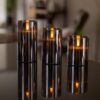 Drie donkergrijze oplaadbare led kaarsen (set van 3), met afstandsbediening en 105 uur brandtijd, staan op een glanzend zwart oppervlak en verspreiden warme weerspiegelingen in een gezellig, modern interieur.
