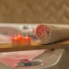 Een opgerolde handdoek en zes oplaadbare waxinelichtjes (RGB, waterdicht, met afstandsbediening en timerfunctie, 68 uur brandtijd) zitten op een houten plank boven een bad gevuld met water voor een ontspannen spa-achtige sfeer.