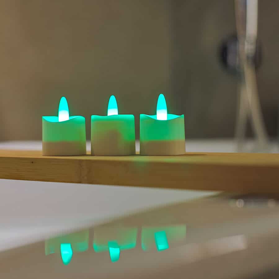 Drie RGB oplaadbare waxinelichtjes, waterdicht en op afstand bestuurbaar met timer en een looptijd van 68 uur, gloeien groen op een houten plank. Hun reflecties verschijnen op een glanzend wit oppervlak; de achtergrond is zacht vervaagd.