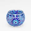 De theelichthouder 9 CM Dorsetto blue is een ronde glazen kandelaar versierd met blauwe, turquoise en paarse geometrische mozaïektegeltjes tegen een witte achtergrond.