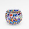 De Theelichthouder 9 CM Dorsetto kleurrijke kraltjes is een ronde glazen waxinelichthouder, versierd met kleurrijke mozaïektegeltjes en kralen in felrode, blauwe, gele, oranje en paarse geometrische patronen op een witte achtergrond.