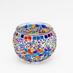 De Theelichthouder 9 CM Dorsetto kleurrijke kraltjes is een ronde glazen waxinelichthouder, versierd met kleurrijke mozaïektegeltjes en kralen in felrode, blauwe, gele, oranje en paarse geometrische patronen op een witte achtergrond.