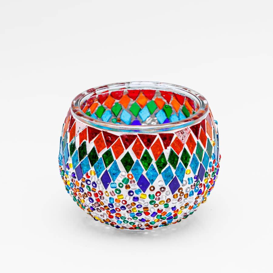 Theelichthouder gekleurde spikkels 9 CM DORSETTO: een ronde glazen kandelaar met levendige rode, groene, blauwe, oranje en gele mozaïeksteentjes en kralen in ruit- en stippatronen op een witte achtergrond.