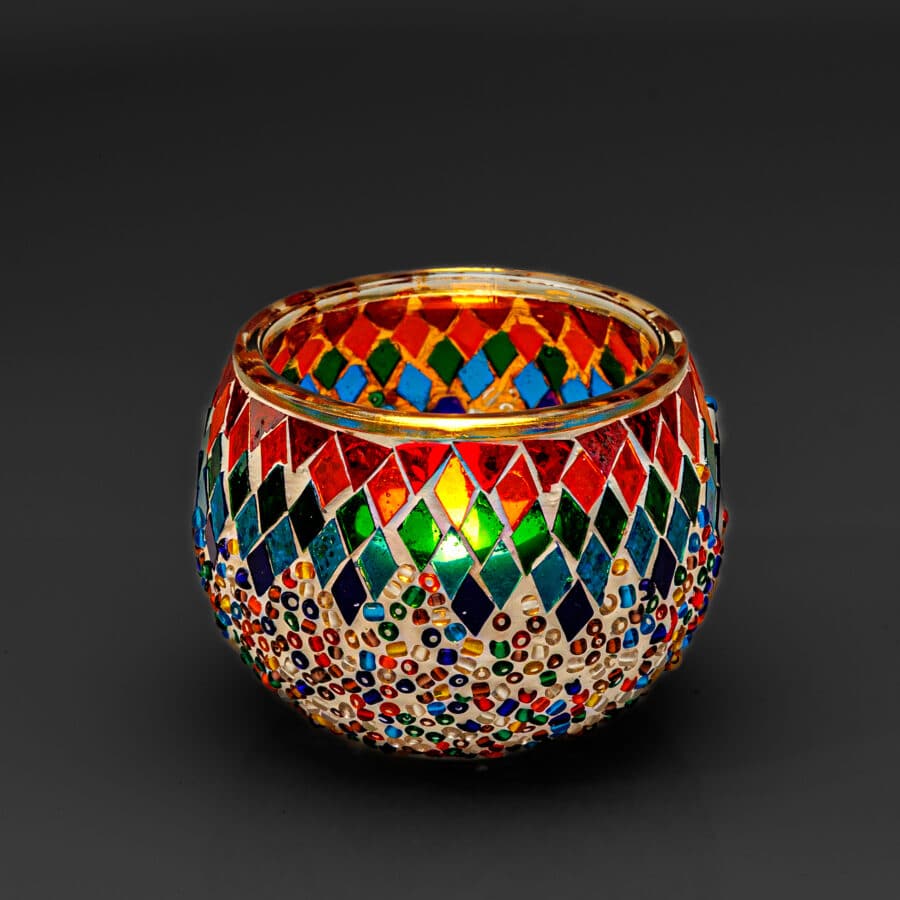 De Theelichthouder gekleurde spikkels 9 CM DORSETTO is een ronde glazen kandelaar versierd met kleurrijke spikkels en ruitpatronen in rood, blauw, groen en goud, tegen een effen zwarte achtergrond.