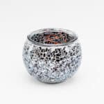 De theelichthouder 9 cm dorsetto beige bruin is een ronde glazen kandelaar met een mozaïek van kleine, onregelmatige spiegelende stukjes in beige en bruin, waardoor een reflecterende en getextureerde look ontstaat tegen een witte achtergrond.