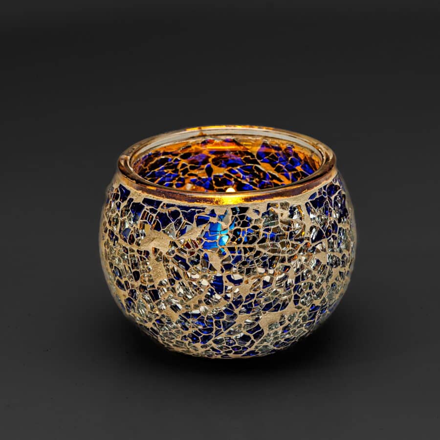 Theelichthouder 9 cm DORSETTO donker blauw: een ronde glazen kandelaar met een mozaïek van blauwe en zilveren stukjes, reflecterend glinsterend oppervlak en gouden rand, afgebeeld tegen een donkere achtergrond.