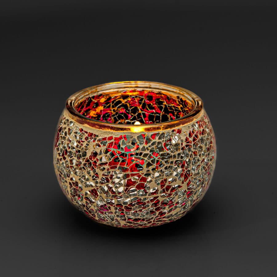 De Theelichthouder 9 cm DORSETTO paars is een ronde glazen waxinelichthouder met een mozaïekontwerp in paarse en spiegelende stukjes, geaccentueerd met goud, tegen een donkere achtergrond.