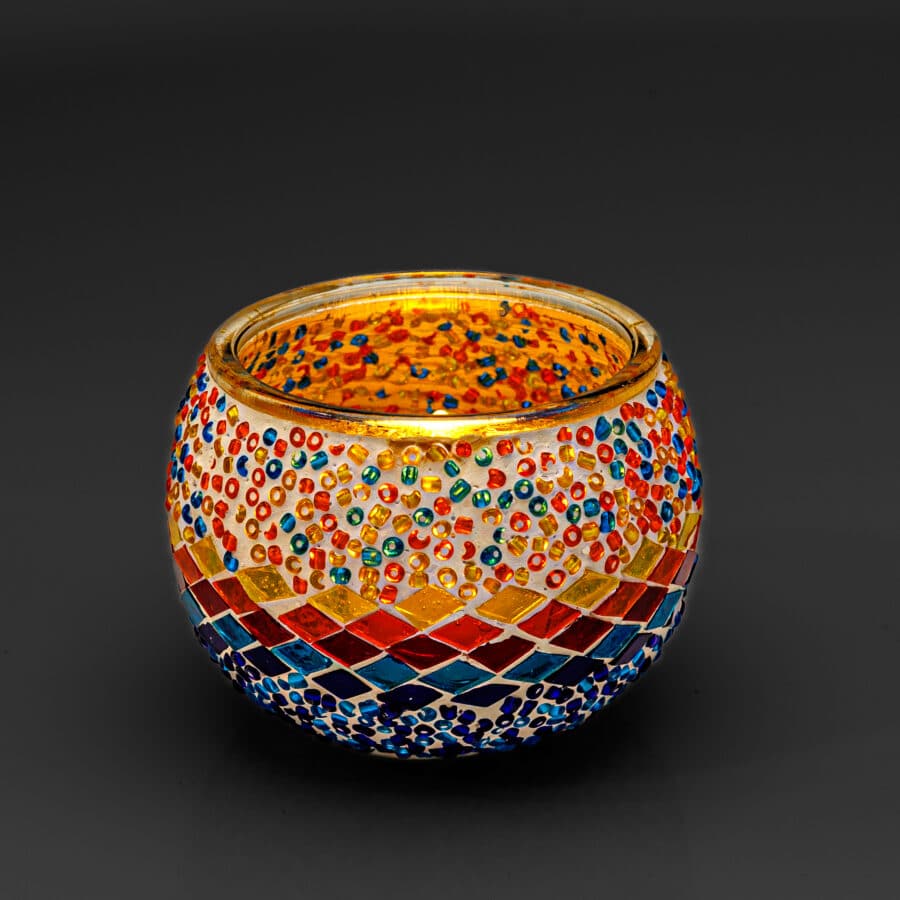 De Waxinelichthouder 9 cm 3 colormix is een ronde glazen kandelaar versierd met levendige mozaïekstukjes en kralen in rood, blauw, geel en groen, tegen een effen donkere achtergrond.