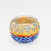 De Waxinelichthouder 9 cm 3 colormix is een ronde glazen kandelaar met kleurrijke mozaïeksteentjes en kralen in rood, oranje, geel, blauw en paars, weergegeven op een effen witte achtergrond.