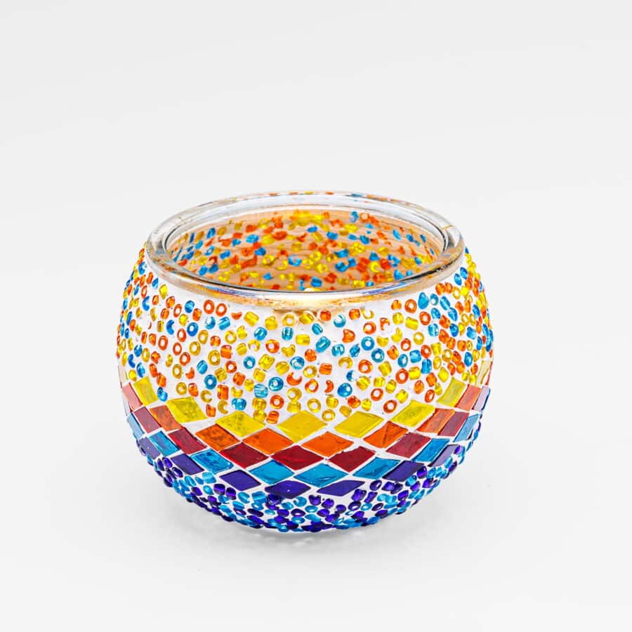 De Waxinelichthouder 9 cm 3 colormix is een ronde glazen kandelaar met kleurrijke mozaïeksteentjes en kralen in rood, oranje, geel, blauw en paars, weergegeven op een effen witte achtergrond.