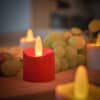 Een close-up van een rode 12 oplaadbare waxinelichtjes led theelichtje met realistisch licht, waterdicht en timerfunctie, brandend tussen groene druiven en andere kaarsen op hout; de achtergrond is zacht vervaagd.