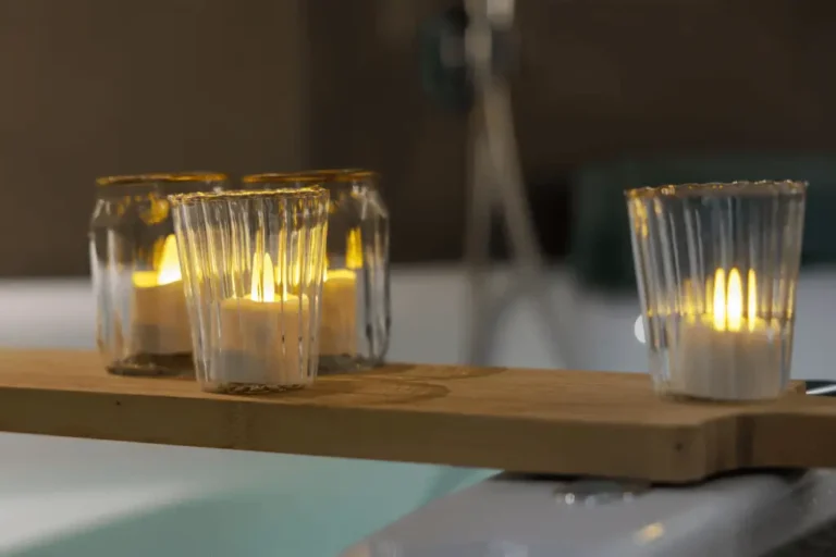 Vier led waxinelichtjes in glazen houders zitten op een houten dienblad boven een bad en creëren een warme en ontspannen sfeer.
