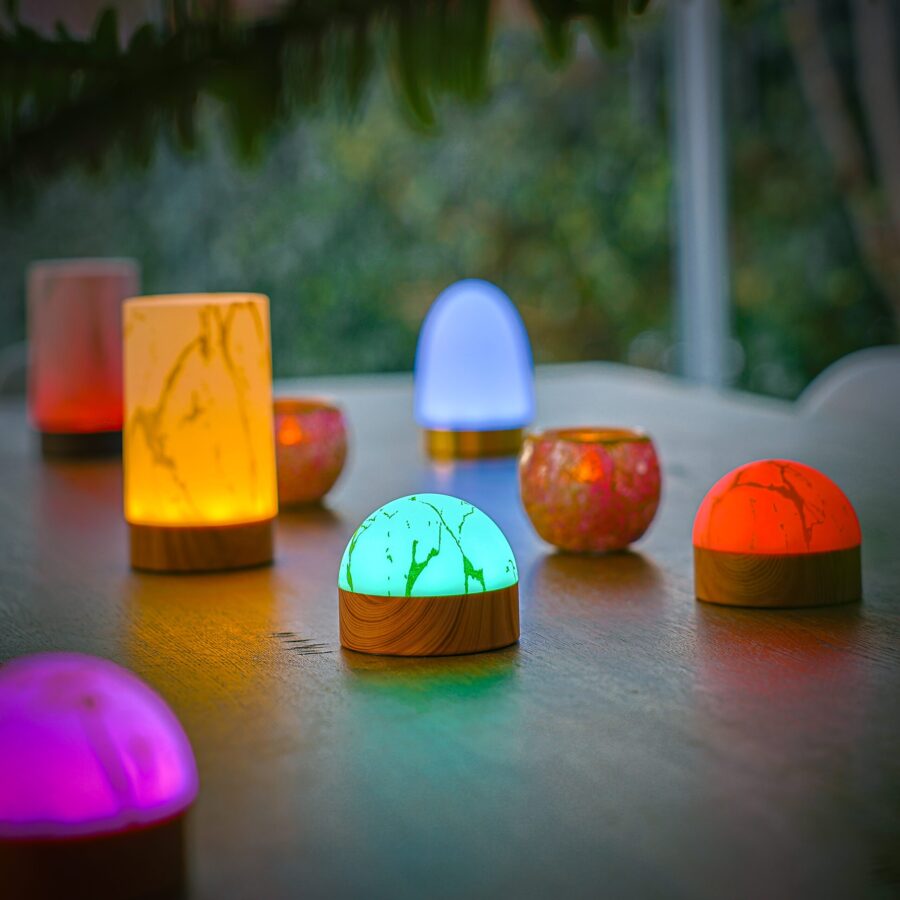 De 1 oplaadbare led tafellamp heeft een waterdicht, koepelvormig ontwerp in wit met een gouden look, timerfunctie en gloeit op een tafelblad tegen een zacht verlichte achtergrond buiten.