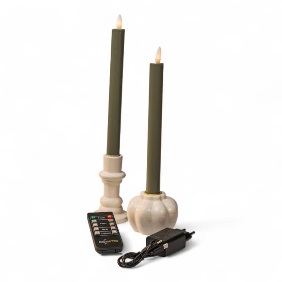 Twee groene conische kaarsen met witte houders, een in de vorm van een pompoen, zijn afgebeeld met een afstandsbediening en een stroomadapter op een witte achtergrond. De kaarsen lijken op batterijen of elektrisch te werken, met nepvlammen.