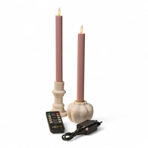 Twee roze LED-kaarsen in witte houders, een afstandsbediening en een zwarte voedingsadapter staan op een witte achtergrond. De kaarsen hebben een zacht, vlamachtig licht aan de bovenkant.