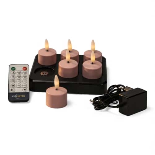 Zes roze elektronische waxinelichtjes met vlamvormige bollen staan op een zwarte oplaadbasis. Een afstandsbediening en een voedingsadapter met kabel liggen naast de voet.