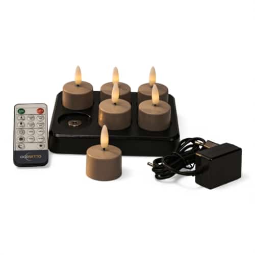 Een set van zes bruine vlamloze LED theelichtkaarsen op een zwart oplaadplateau, met een afstandsbediening en een zwarte voedingsadapter ernaast geplaatst.